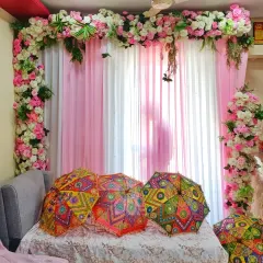A sweet and simple baby welcome decoration at home, using a pink and white floral arch and decorative umbrellas over a sofa.