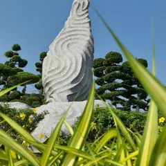A close-up of a custom-carved stone sculpture, designed to mimic the flow of water. This piece serves as a focal point amidst the sculpted topiary and lush greenery of the Hyderabad garden.