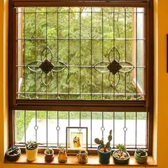 This window detail from the Roopa Hariprasad Residence showcases the delicate floral motif of the security grille. Paired with a collection of potted succulents on the sill, it demonstrates how functional elements can enhance a home's aesthetic.