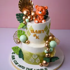 Welcoming a new cub into the world with this adorable tiger-themed baby shower cake. The two-tier design features jungle leaves, gold and green spheres, and a cute little fondant tiger sitting on top.