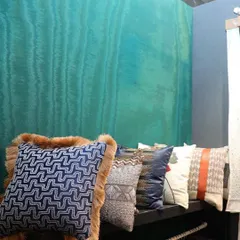 A row of our bespoke cushions displayed against a vibrant turquoise wall. The collection features a variety of patterns, including geometric mazes and abstract prints, with luxurious details like fur-trimmed edges, showcasing the diversity and quality of our custom accent pieces.