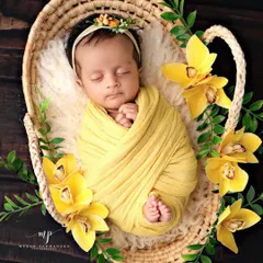 The definition of peaceful slumber. This newborn is swaddled snugly in a vibrant yellow wrap, nestled in a rustic basket and surrounded by beautiful matching flowers, showcasing our classic posed photography style.