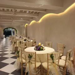 Indoor seating for a Parsi union at Colaba Agiary. The round tables are dressed in cream linens, with gold chiavari chairs decorated with sheer sashes, complementing the venue's classic black and white checkered floor.