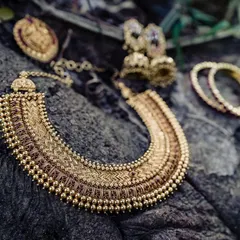 An artistic flat lay of the bride's temple jewelry on a piece of textured wood. This shot highlights the intricate craftsmanship of the traditional gold necklace, earrings, and bangles.