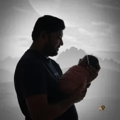 A striking black and white silhouette of a father holding his newborn against a softly lit background. The image is dramatic, emotional, and timeless.