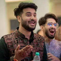 A candid shot of the groom and a friend reacting with excitement during a performance. Capturing guest reactions is key to telling the full story of the event.