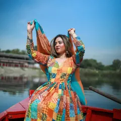 A playful shot of the model on the boat, holding her dupatta up against the clear blue sky.