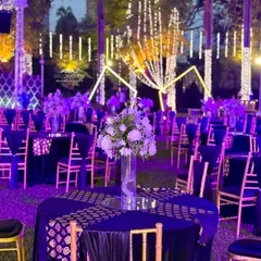 Elegant guest seating for a Sangeet, with deep blue tablecloths, gold-patterned runners, and simple floral centerpieces under a canopy of lights.