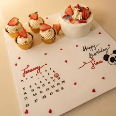 A creative and personalized birthday gift set. This features a small strawberry cake, matching cupcakes, and a hand-piped calendar on the board marking the special day, January 11th.