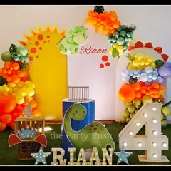 This dinosaur theme for Riaan's 4th birthday uses bright, fun colors. The decor features cute dinosaur cutouts, a sun-shaped backdrop, and a large marquee number '4'.