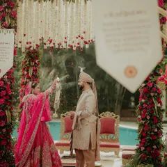 A wide shot of the playful Varmala exchange. This image shows the bride tossing petals at her groom, a fun and candid moment set against the beautiful poolside mandap.