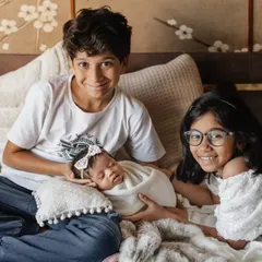 A full house and a full heart. This lifestyle portrait shows older siblings proudly gathered around their new baby sister on the family bed, a beautiful moment of togetherness.