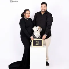 A modern family portrait with a pet. The couple and their stylishly dressed dog pose for a clean, minimalist shot against a white studio background.