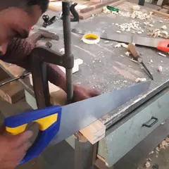 With a piece securely clamped, a student focuses on making a straight and accurate cut with a hand saw, a core skill for creating strong joinery.