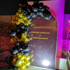 I design branded backdrops for corporate milestones, like this one for a company celebrating 100k followers. The design includes a custom printed backdrop with the company's message, framed by a stylish black and gold organic balloon garland.