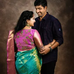 A classic maternity portrait of a couple in traditional Indian attire. The mom-to-be wears a vibrant turquoise and pink silk saree, showcasing the elegance of a traditional pregnancy photoshoot.