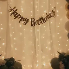 A simple and elegant backdrop created with a curtain of fairy lights. A "Happy Birthday" banner is hung across the top, creating a warm and inviting atmosphere for a home celebration.