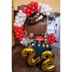 We help you celebrate every milestone, like this 22nd birthday. This cozy home setup features large gold foil balloon numbers, a red and white balloon arch, and a decorated table ready for the cake cutting.