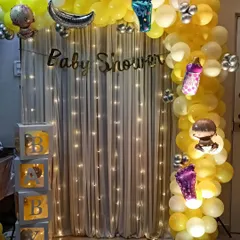 A classic baby shower decoration with a yellow and white color scheme. This setup includes transparent 'BABY' boxes and a fairy light backdrop for a simple yet elegant look.