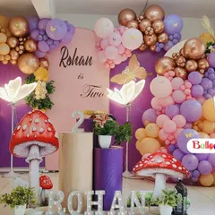 An enchanting fairy garden theme for a second birthday party. This decoration features a pastel balloon arch with rose gold accents, giant mushroom props, illuminated flowers, and a large marquee number '2'.