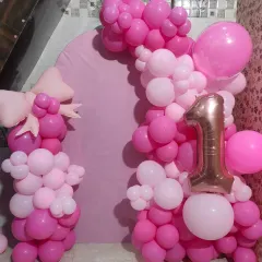 A pink-themed first birthday photo booth with a large '1' foil balloon and a cute bow accent.