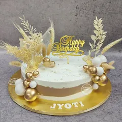 A stunning boho birthday cake. The design features a mix of gold and white spheres, dried grasses, and a gold "Happy Birthday" topper for a trendy and celebratory feel.