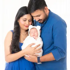 A tender moment between new parents and their baby, who is dressed in an adorable white bear bonnet.