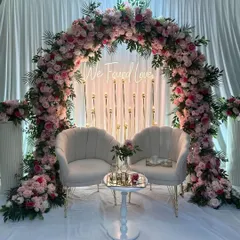 A dreamy Roka ceremony backdrop featuring a full floral arch of pink roses, a 'We Found Love' neon sign, and soft candlelight for a romantic ambiance.