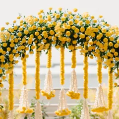 A close-up of a Haldi floral arch, showing the detail of the bright yellow flowers and traditional white tassels.