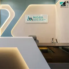 A close-up of the bespoke reception desk for Misba Holidays. The angular, minimalist design in white solid surface is accented with under-counter lighting, creating a floating effect that is both modern and welcoming.