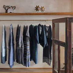 Clothing is displayed on simple wooden shelves with brass hanging rods, set against textured, lime-washed walls. The material palette is intentionally timeless, using natural wood and concrete to feel both refined and warm.