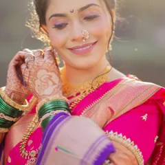 A candid moment of the bride adjusting her earring. This shot highlights the soft, shimmery eye makeup, the delicate nath, and the beautiful green glass bangles, all essential parts of the 'Marathmola' look.