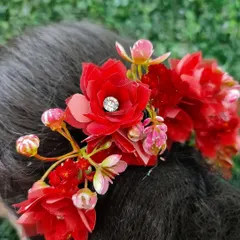 A vibrant red floral hair veni, perfect for a traditional bride. The delicate red flowers are accented with a single crystal for a touch of sparkle.