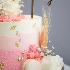 A close-up of the textures on the blush and gold cake, from the piped buttercream details to the smooth ombre frosting and delicate macarons.
