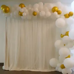 A simple and elegant balloon decoration featuring a white and gold partial arch against a white curtain. This minimalist design is perfect for sophisticated celebrations.