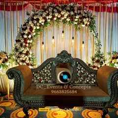 A beautiful engagement stage setup with a floral arch of red and white roses, complemented by an ornate traditional sofa and hanging industrial-style bulbs.