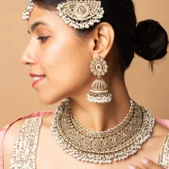 A profile shot showcasing a complete bridal jewellery set, including the maang tikka, passa, jhumkas, and necklace, against a soft, neutral background.