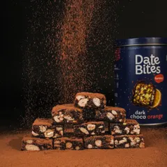 A dramatic shot of cocoa powder being dusted over a stack of Date Bites. Using a dark background makes the action pop and creates a rich, moody atmosphere.