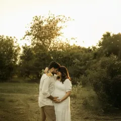 A quiet moment of connection against the backdrop of a setting sun. The warm light and natural surroundings create a peaceful, romantic atmosphere for this outdoor couple maternity portrait.