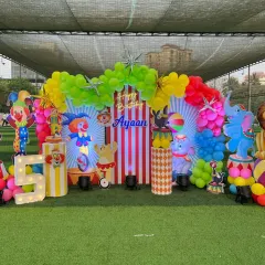 We created a full-scale carnival theme for this outdoor 5th birthday party. The setup includes a vibrant balloon arch, life-sized cutouts of circus animals and clowns, and custom-striped pedestals for a truly immersive experience.
