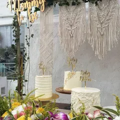The details of a boho-themed baby shower, featuring a custom macrame art piece and a trio of elegant cakes. The 'Mommy to be' sign adds a lovely, personal touch to the dessert table.