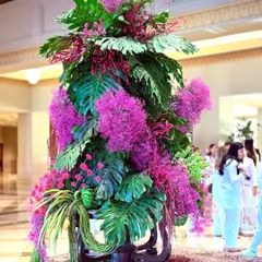 The beauty of this piece is in its texture and scale. The interplay between the broad green leaves and the delicate clusters of pink flowers creates a dynamic and visually captivating floral sculpture.