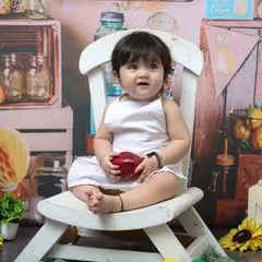Holding an apple in a charming, rustic setup, this one-year-old is the star of his birthday shoot. The white chair and fruit-stand background create a wholesome and sweet portrait.