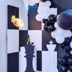 This clever chess-themed decor is perfect for someone who loves strategy and style. The black and white checkerboard backdrop and giant chess piece props create a bold and unforgettable party look.