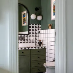 A peek into a bathroom from the 'Inde Blue' project reveals a space rich in color and pattern. The olive green vanity, geometric tiles, and modern globe lighting create a look that is bold, graphic, and full of personality.