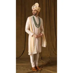 A full-length view of the 'Jashn-e-Ada' sherwani in a soft blush peach. The handwoven fabric is adorned with delicate threadwork and a hint of gold, creating a look of contemporary regal charm.