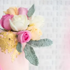 A close-up of the floral arrangement on this elegant two-tiered cake. A mix of pink, white, and peach roses is accented with gold-dusted leaves, creating a look of baked-in elegance.