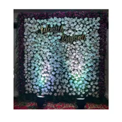 An elegant floral backdrop for a naming ceremony. The wall is densely packed with white and purple flowers, with the baby's name in a golden script at the center.