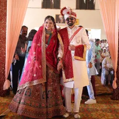 A happy bride and groom making their entrance as a married couple. She is glowing in a beautiful multi-toned bridal lehenga, perfectly complementing his sherwani.