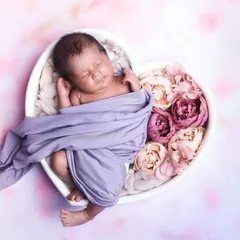 A beautiful pose with a baby partially wrapped in a lavender cloth, sleeping in a heart-shaped bowl filled with flowers.